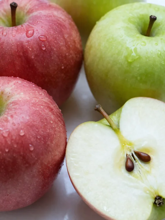 Fresh red and green apples on a cutting board, sliced and whole, with apple juice
