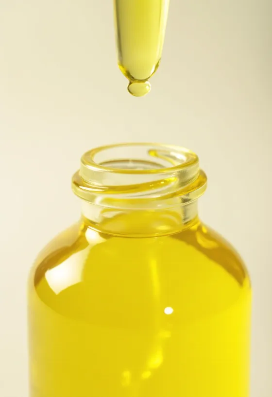 Lemon oil in a small bottle, next to fresh lemon slices and grated zest