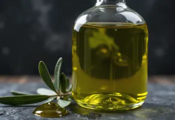 Extra virgin olive oil in a clear glass bowl, golden-green color, on a white background