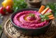 Smooth beet hummus served in a bowl with a swirl of olive oil