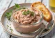 Creamy liver pate spread on fresh bread garnished with herbs.